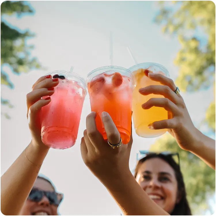 Three people holding up colorful iced drinks outdoors on a sunny day.