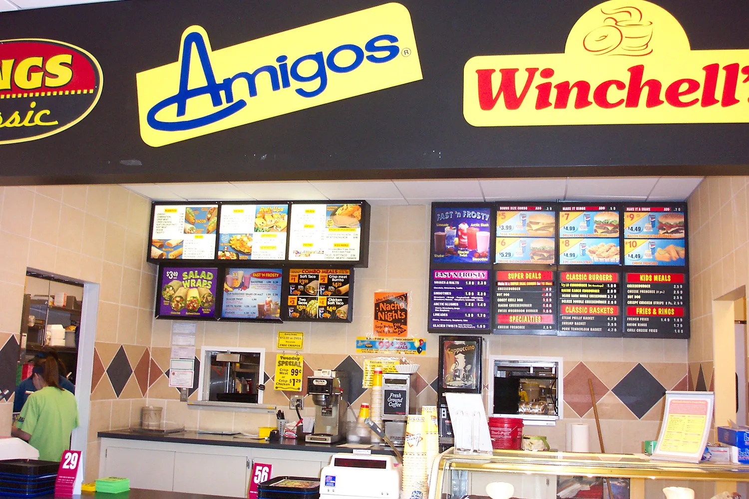 Building with signs for Amigos Mexican Food and Church's Chicken, with a banner saying Now Open and parked cars in front.