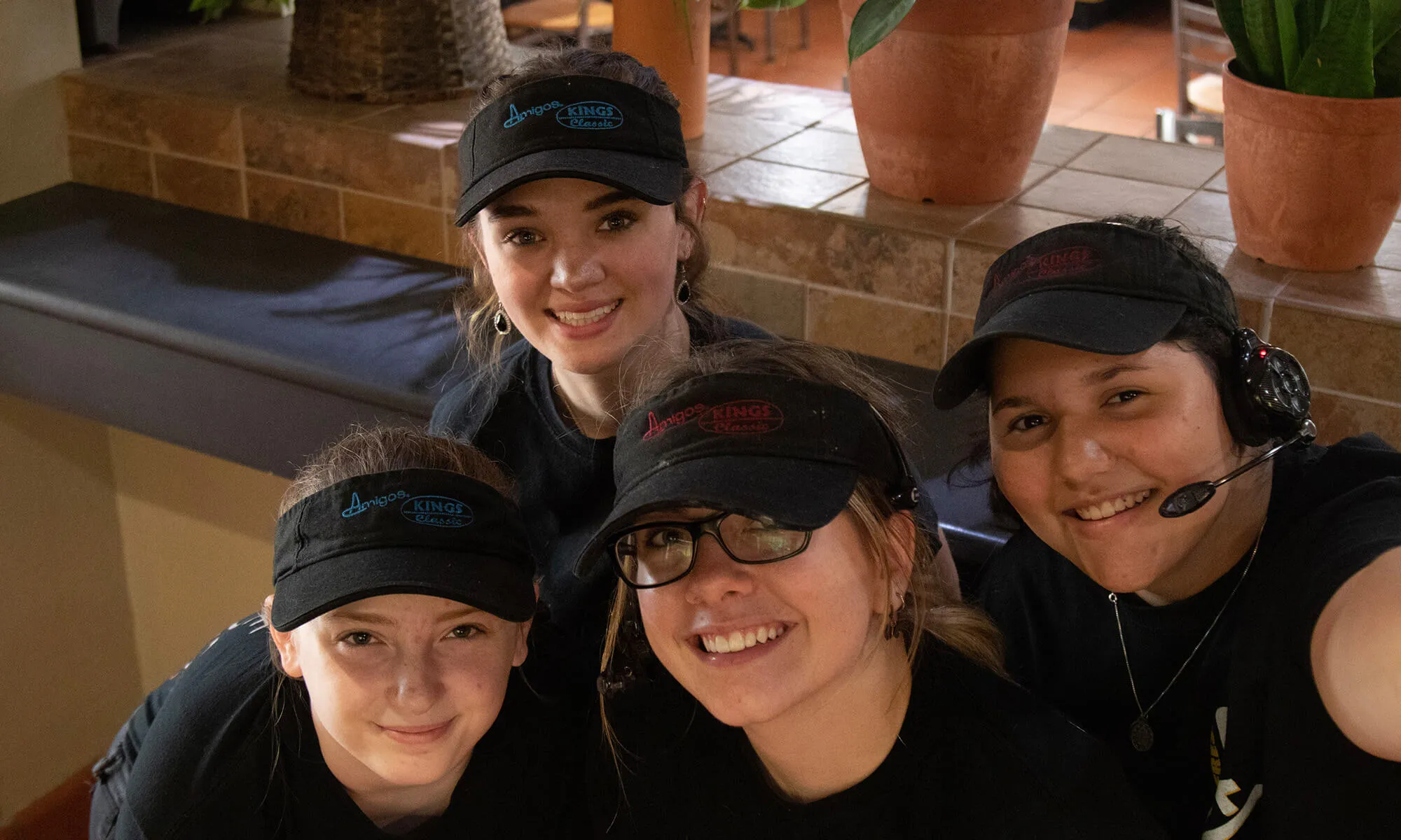 Four smiling individuals wearing black caps and headsets are gathered closely. They appear friendly and approachable, suggesting a positive work environment.