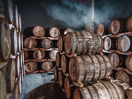 Stacked wooden barrels in a dimly lit cellar with smoke or mist in the background.