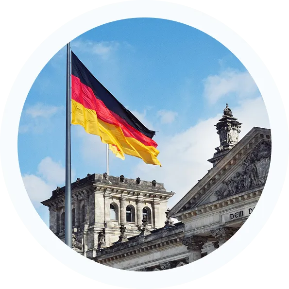 German flag flying atop the Reichstag building against a partly cloudy blue sky.