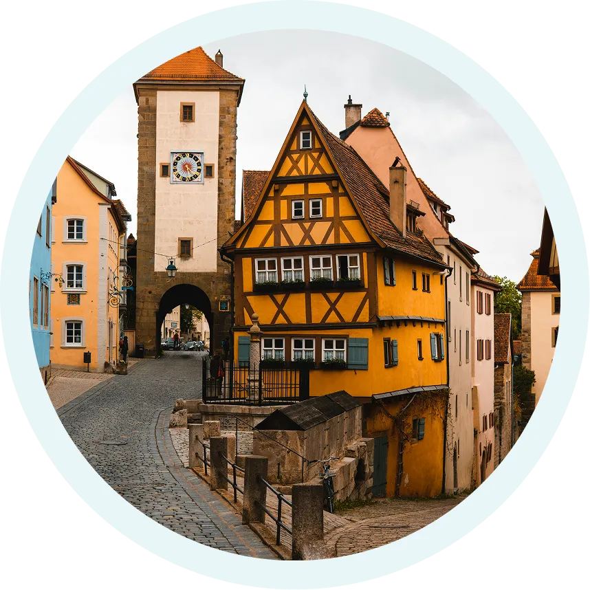 Cobblestone street in a European town with a yellow half-timbered house and a clock tower archway.