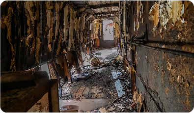 Interior of an abandoned, dilapidated corridor with peeling walls and debris on the floor.