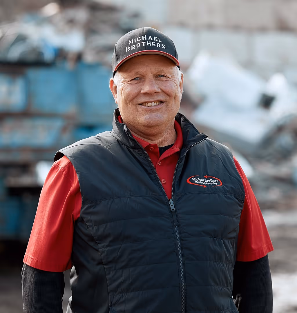 Steve wearing a black Michael Brothers cap and vest over a red shirt standing outdoors.