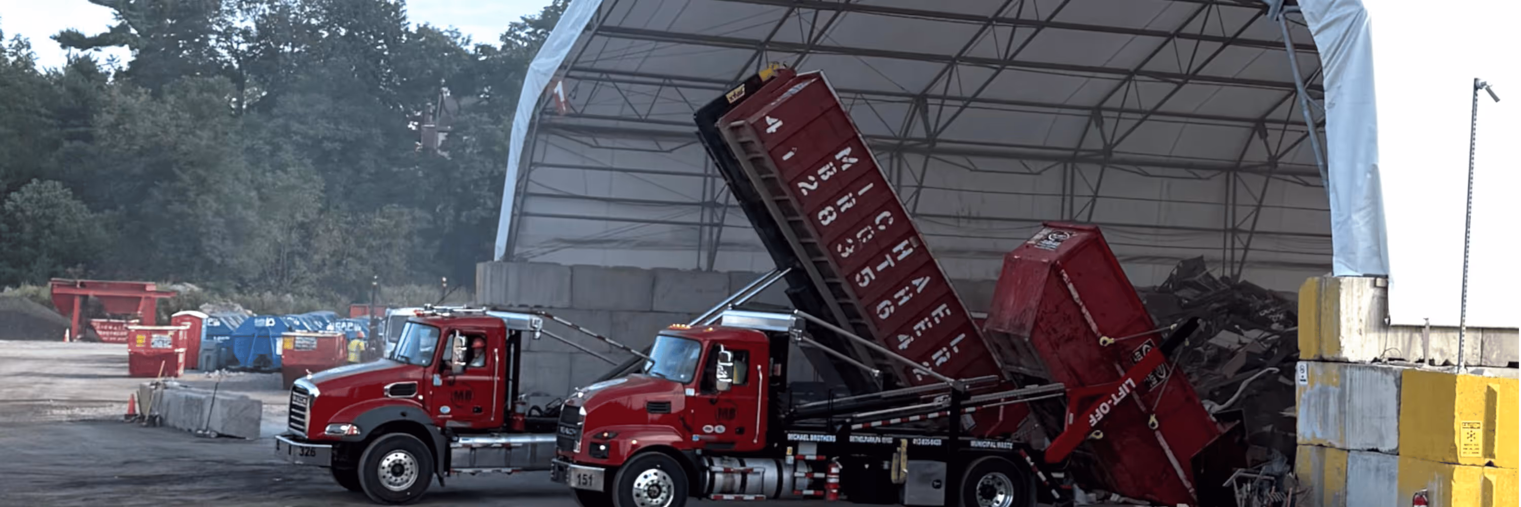 Red trucks unloading large red dumpsters filled with debris at an outdoor recycling facility.