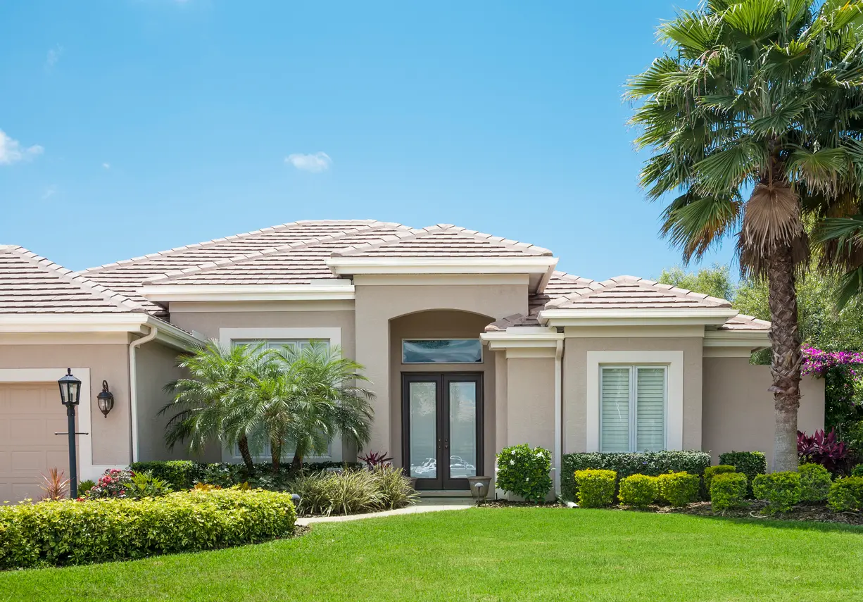 Modern house with beige stucco walls, tile roof, palm trees, and beautiful yard in Bonita Springs.