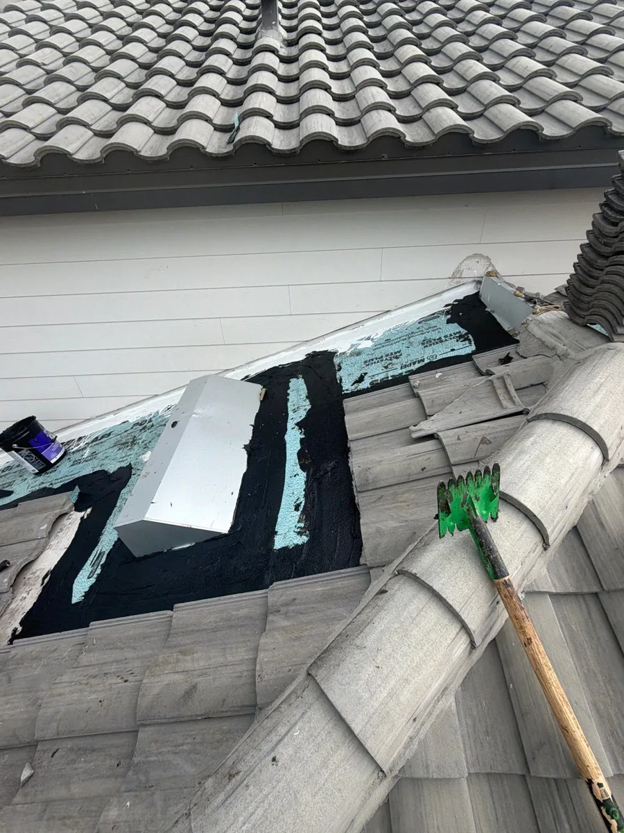 Roof-to-wall repair in progress with tiles lifted and the waterproofing and flashing exposed