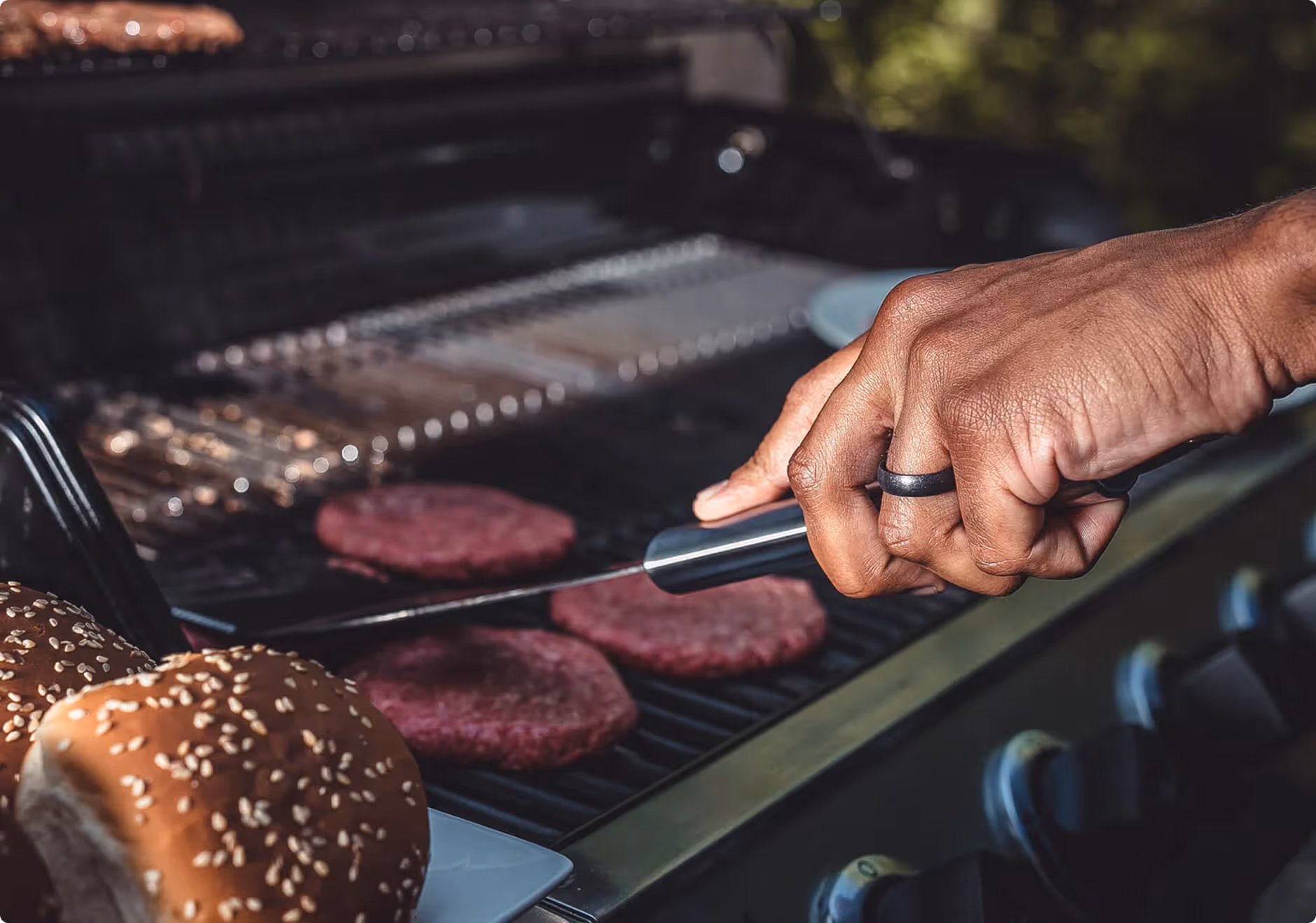 A person is cooking hamburgers on a grill.