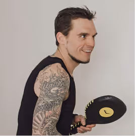 Junger Mann mit Ärmel-Tattoo trainiert mit einem schwarzen Tischtennisschläger.