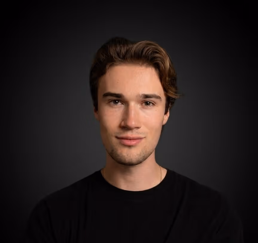 Porträt eines jungen Mannes mit braunen Haaren vor dunklem Hintergrund.