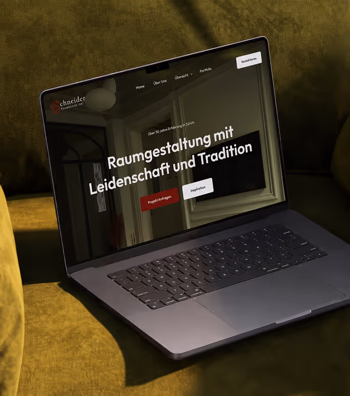 Laptop auf grünem Sofa mit Webseite von Schneider Raumgestaltung in Deutsch angezeigt.