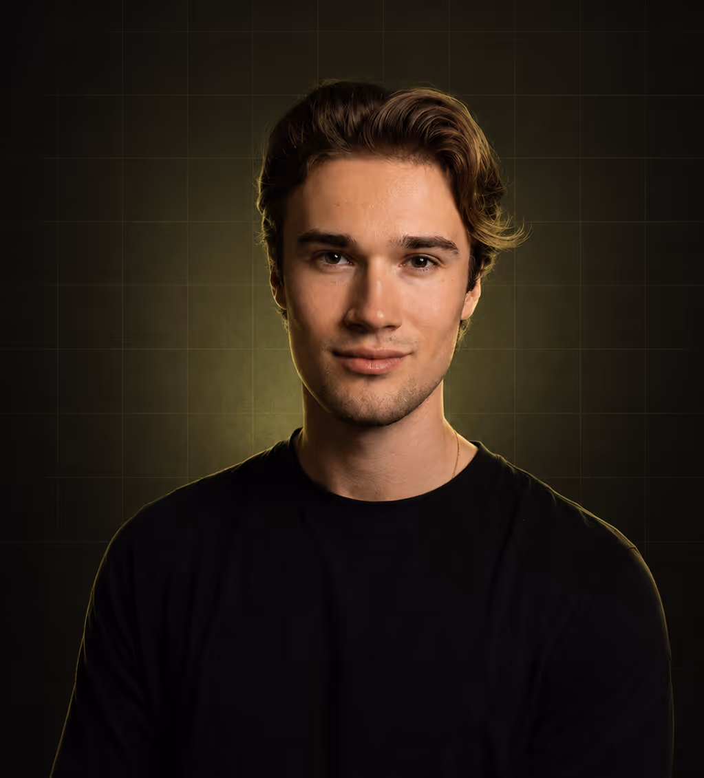 Porträt eines jungen Mannes mit braunen Haaren und schwarzem T-Shirt vor dunklem Hintergrund.