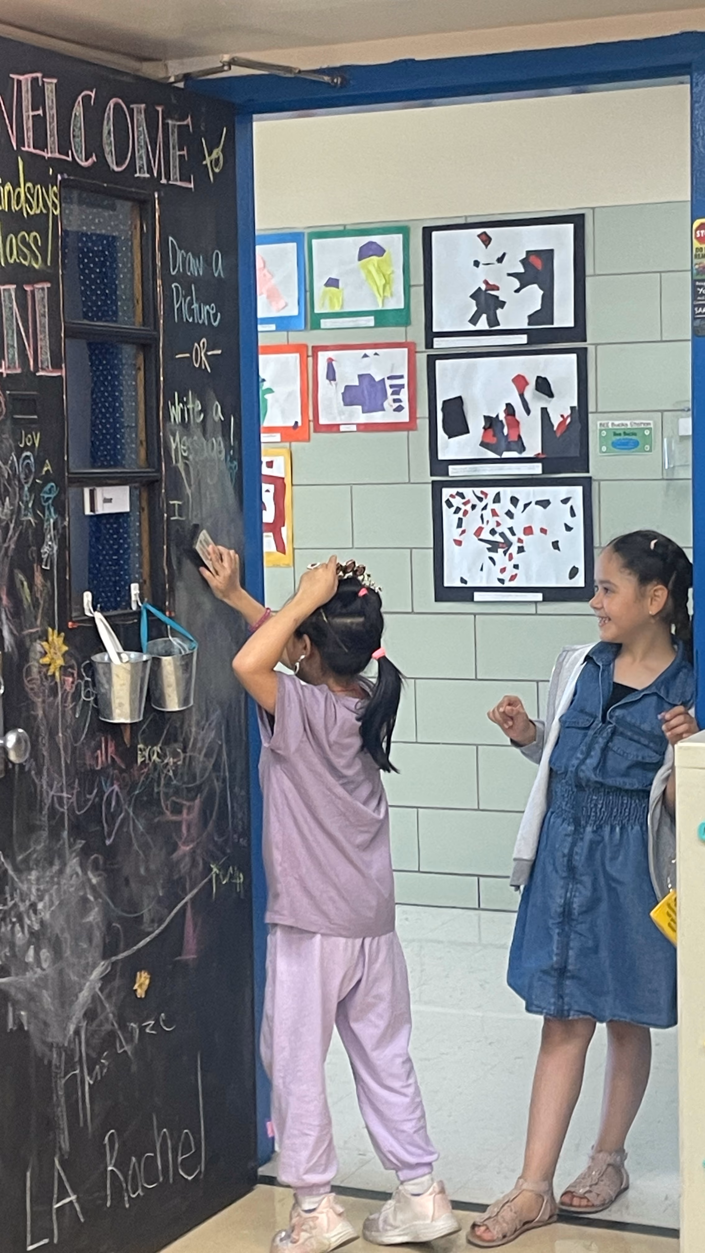 Student writing on classroom chalkboard while classmate watches