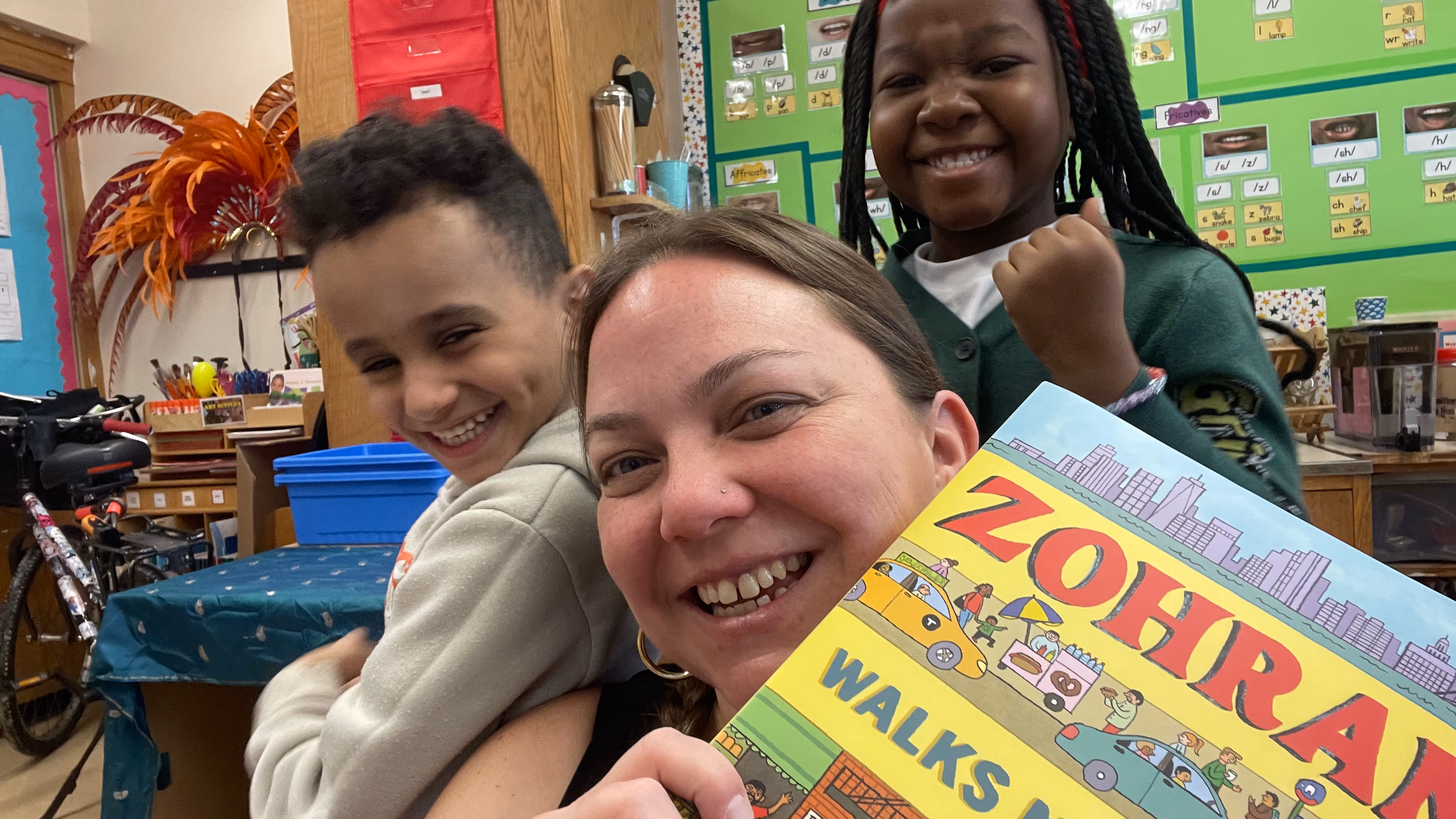 Teacher and two students smiling with classroom book