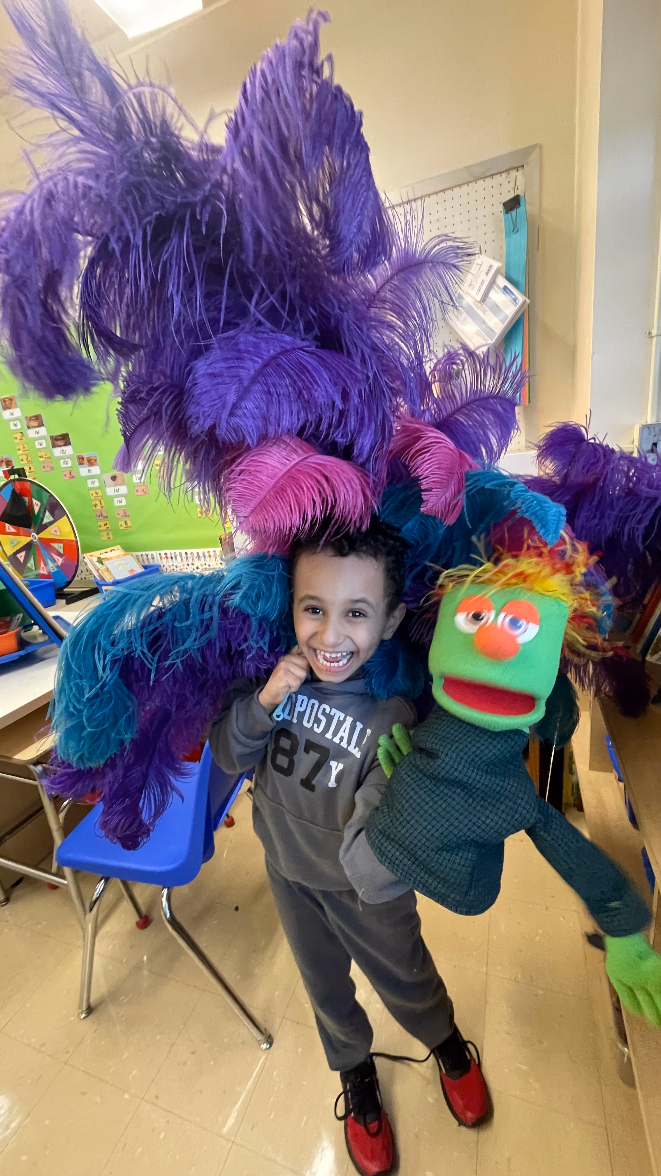 Student holding colorful feathered costume and puppet