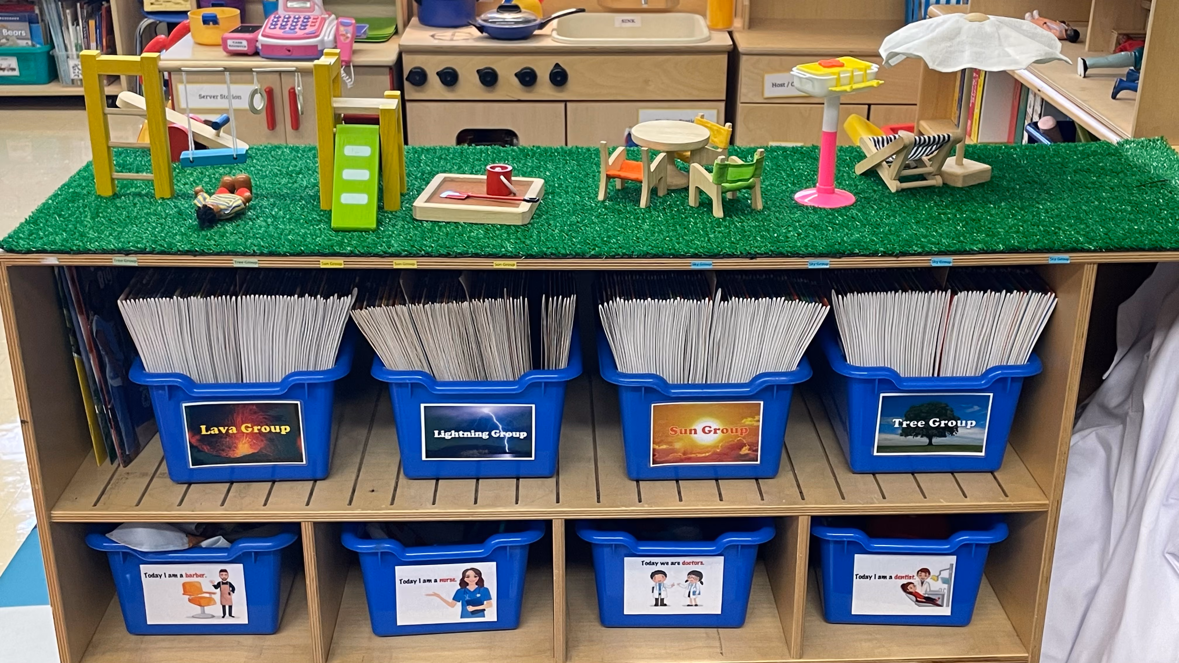 Organized classroom storage with labeled student group bins and miniature play scene