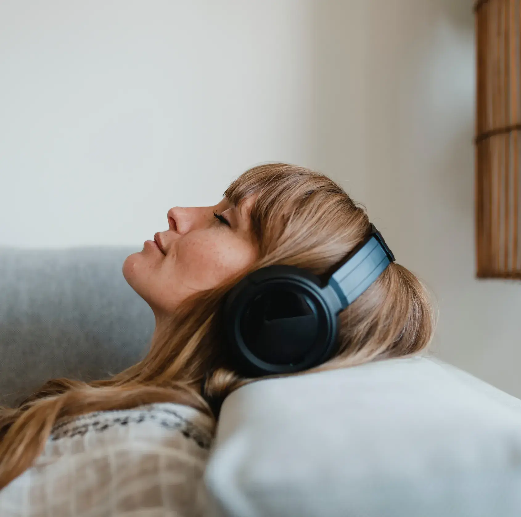 A person with long hair relaxes on a couch, wearing large black headphones.