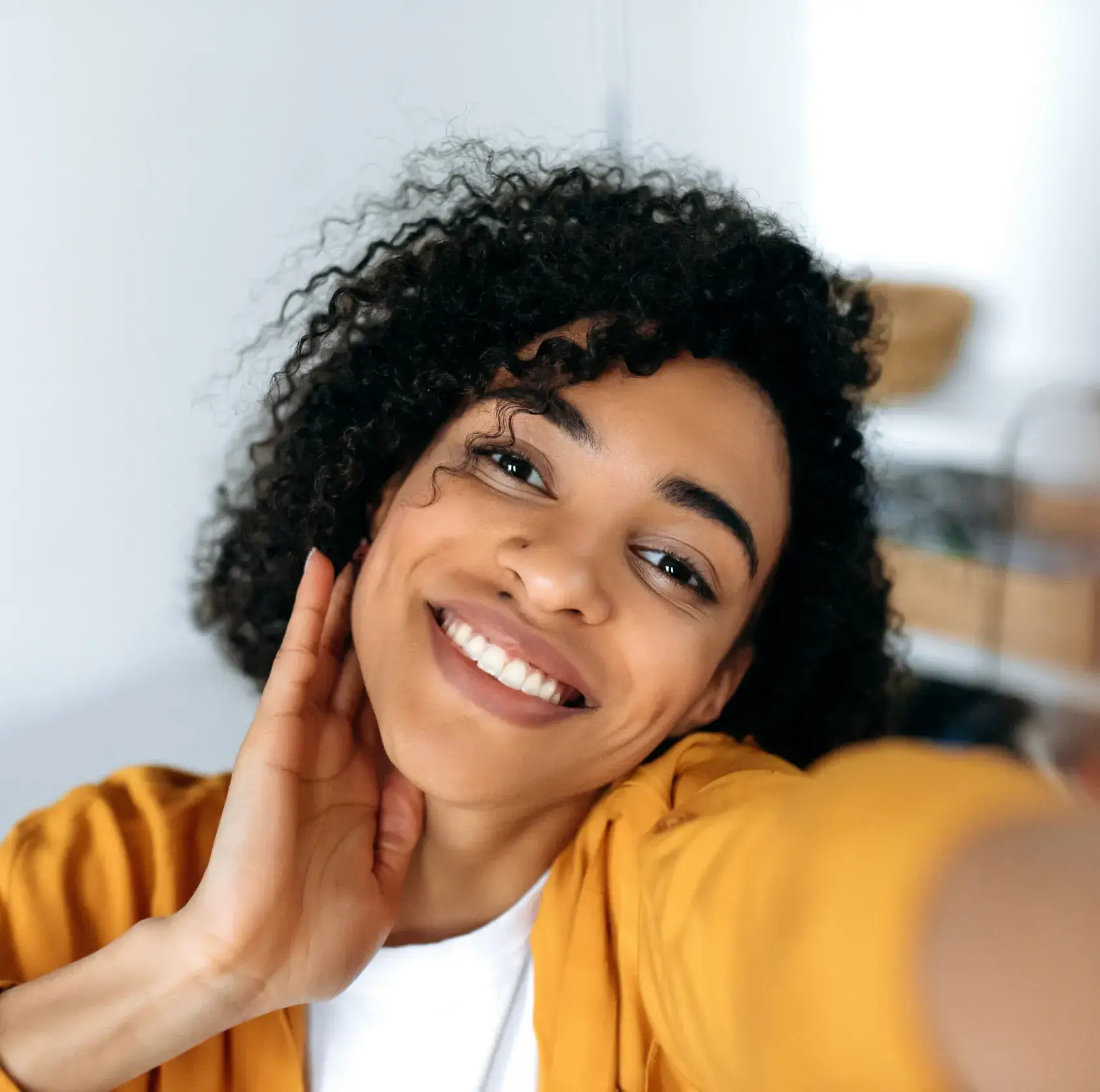 A person with curly hair smiles while taking a selfie indoors.