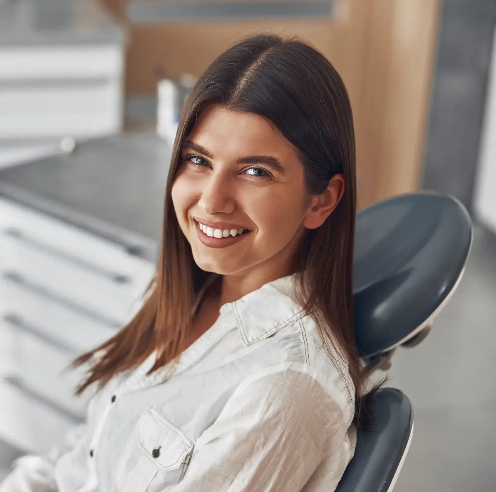 A woman with long hair smiles while sitting in a dentist's chair.