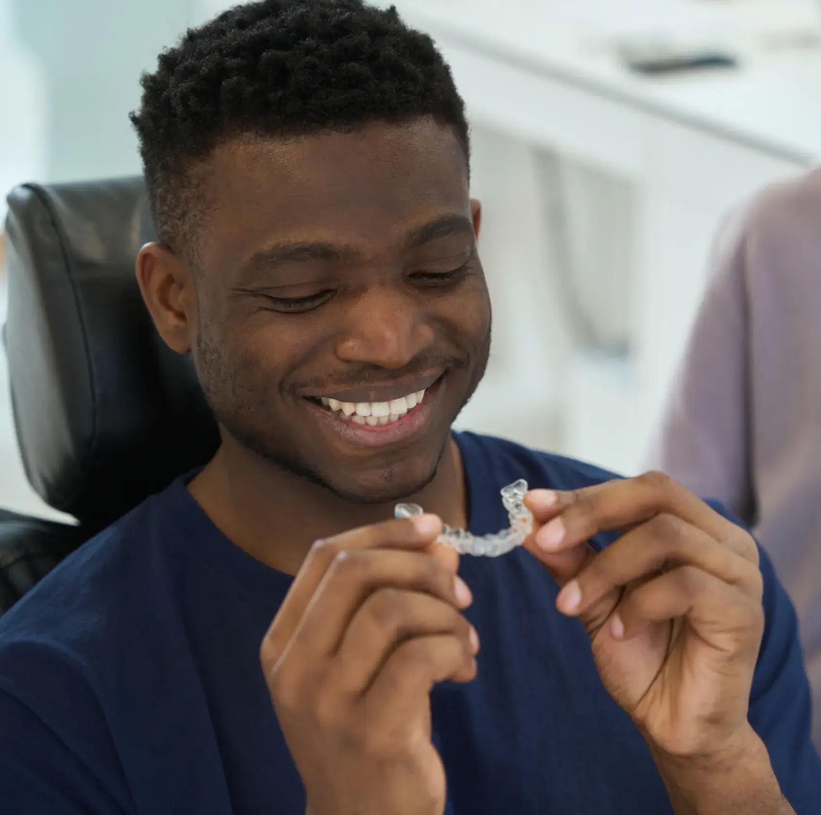 Man smiling and holding a clear dental aligner in his hands.