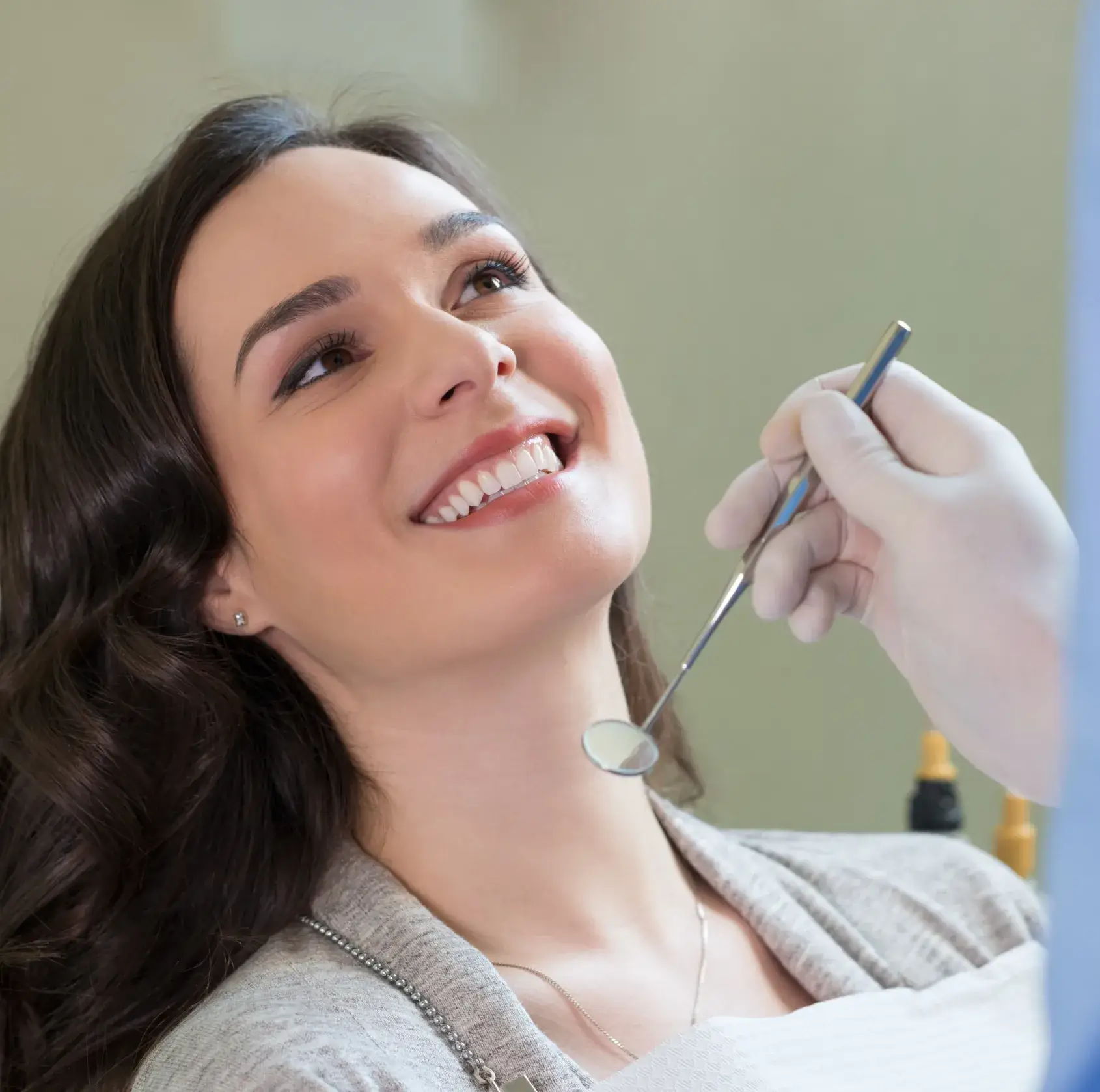 A woman smiles while a dentist holds a dental mirror near her mouth.