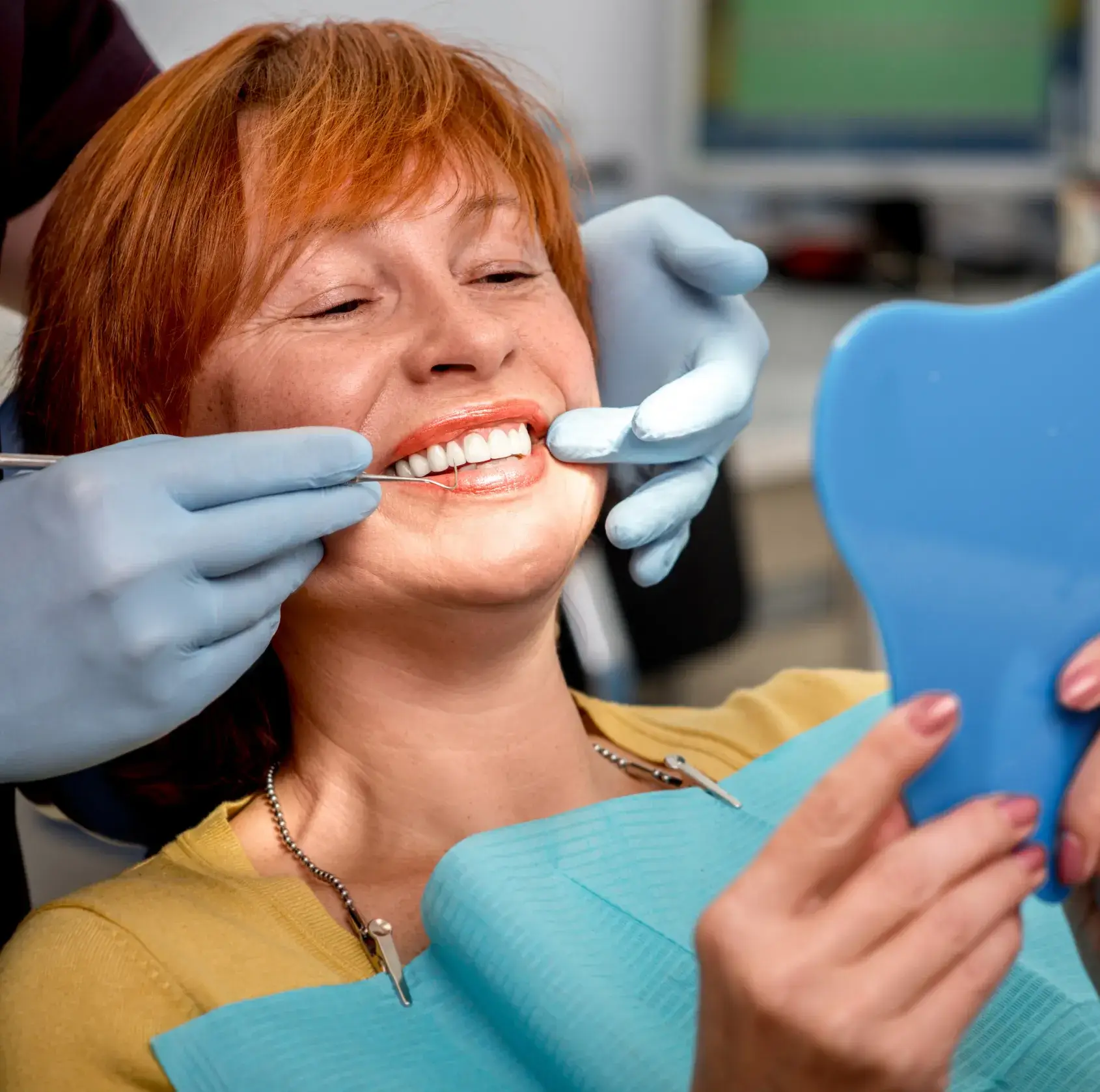 A woman at the dentist, smiling while holding a small mirror, as the dentist examines her.