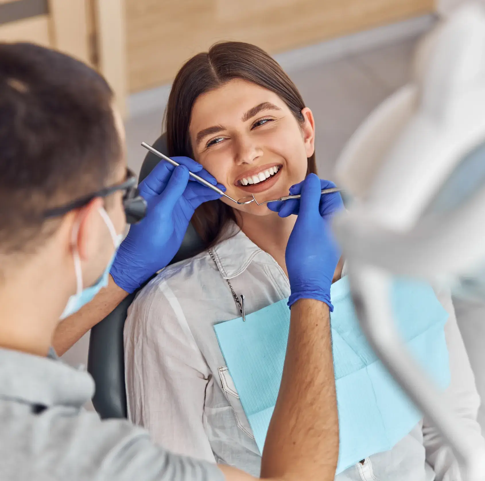 Dentist examines a smiling woman's teeth with a dental tool.