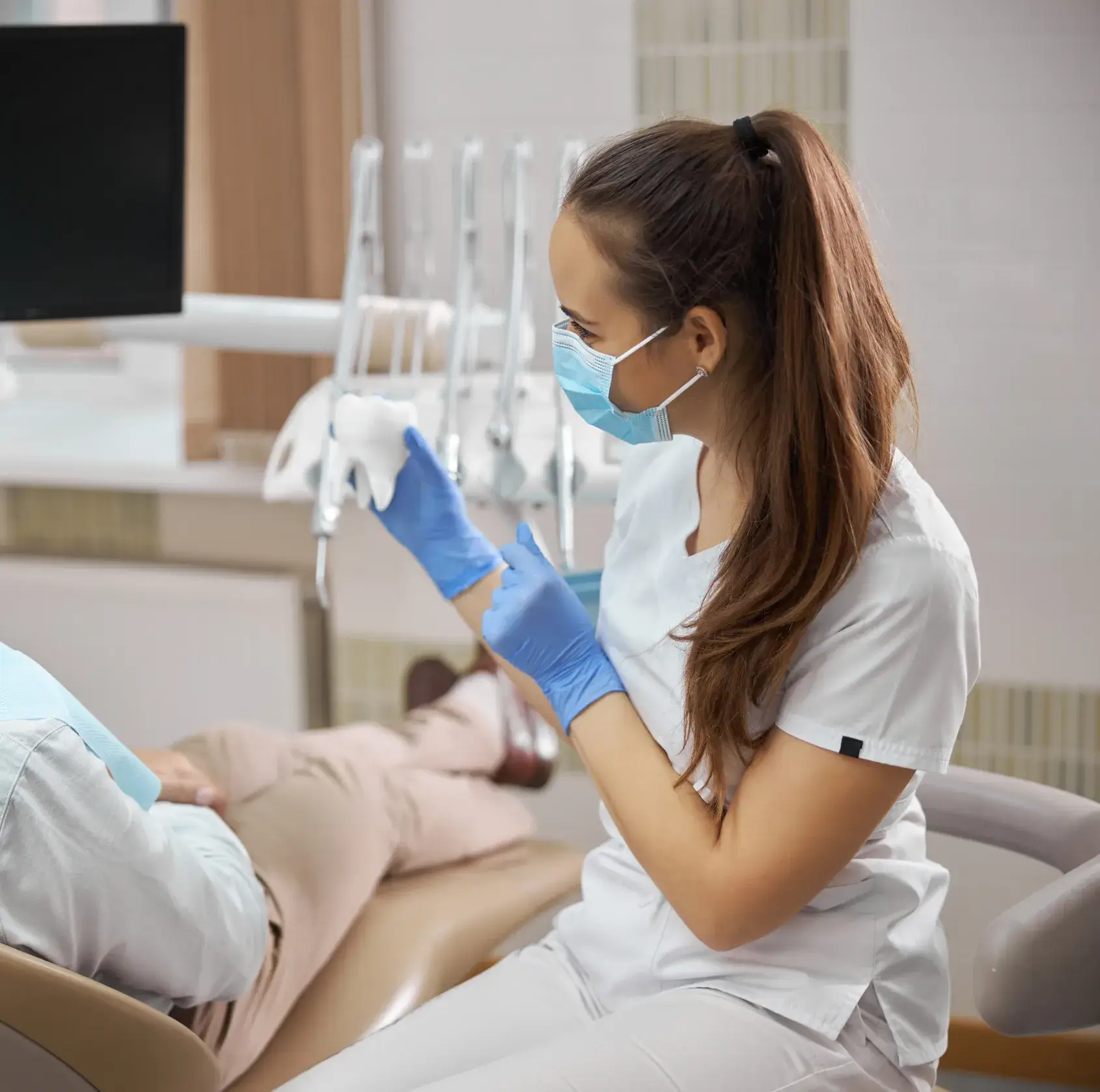 A dental assistant in a mask and gloves shows a patient a dental mold.