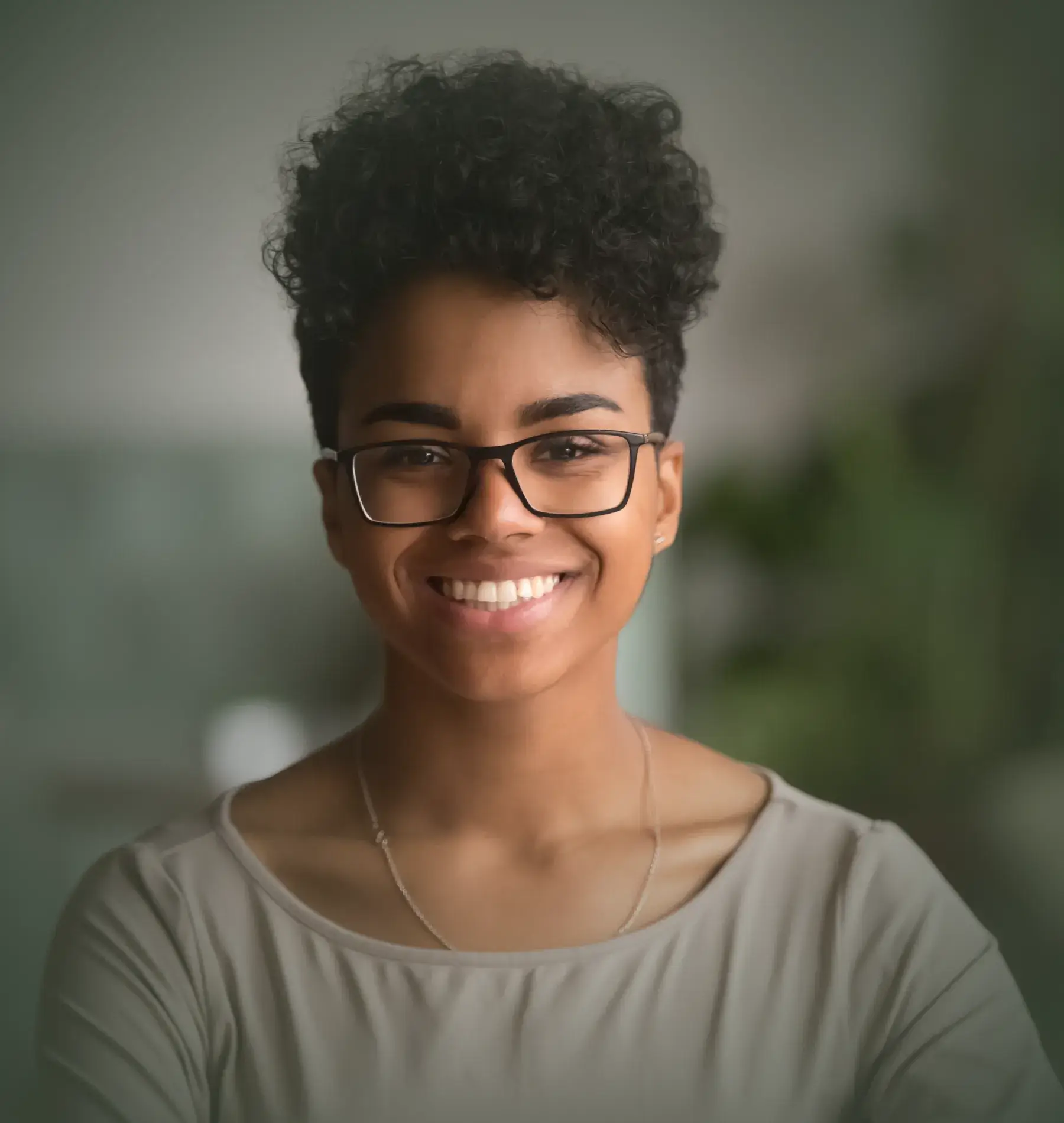 Person smiling and wearing glasses, standing in a softly lit room.