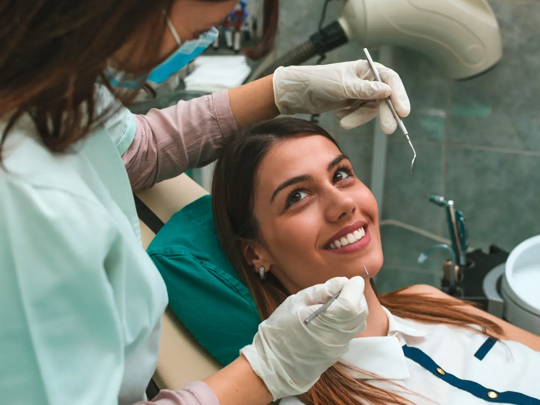 A dentist examines a smiling woman in a dental chair with dental tools.