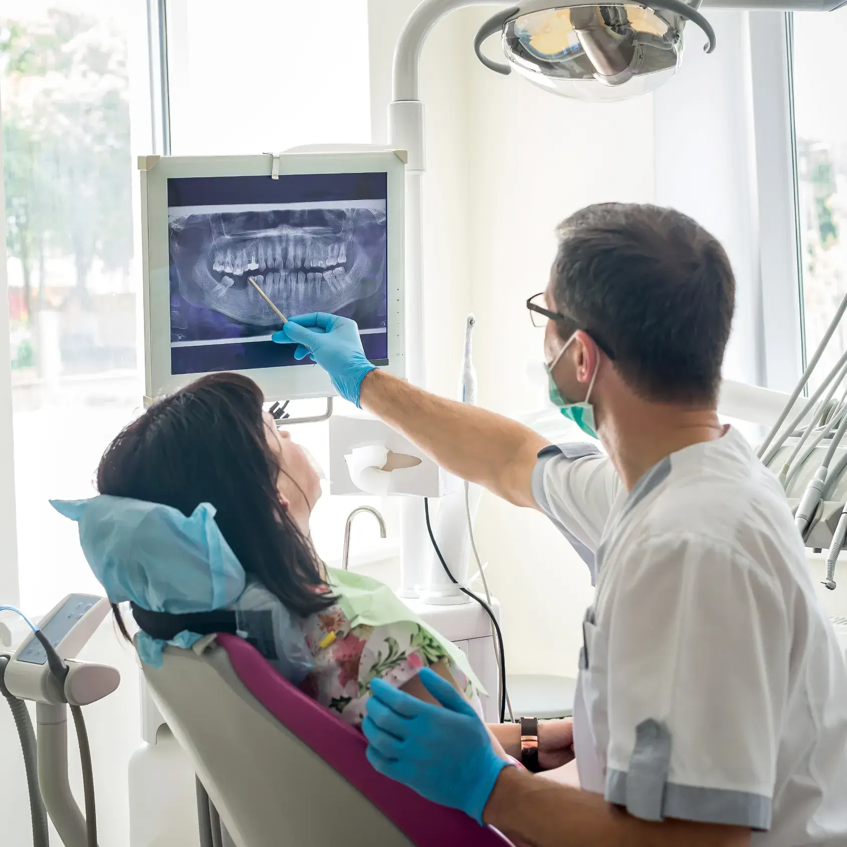 A dentist shows a dental X-ray to a patient sitting in a chair.