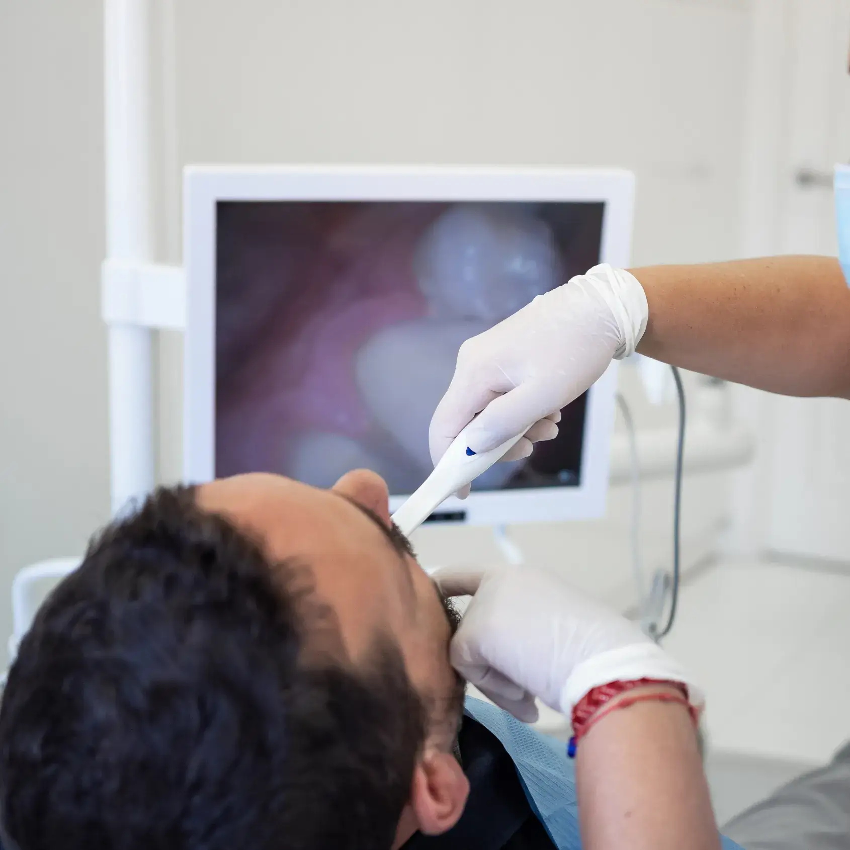 A dentist examines a patient's teeth using an intraoral camera, with a screen displaying the image.