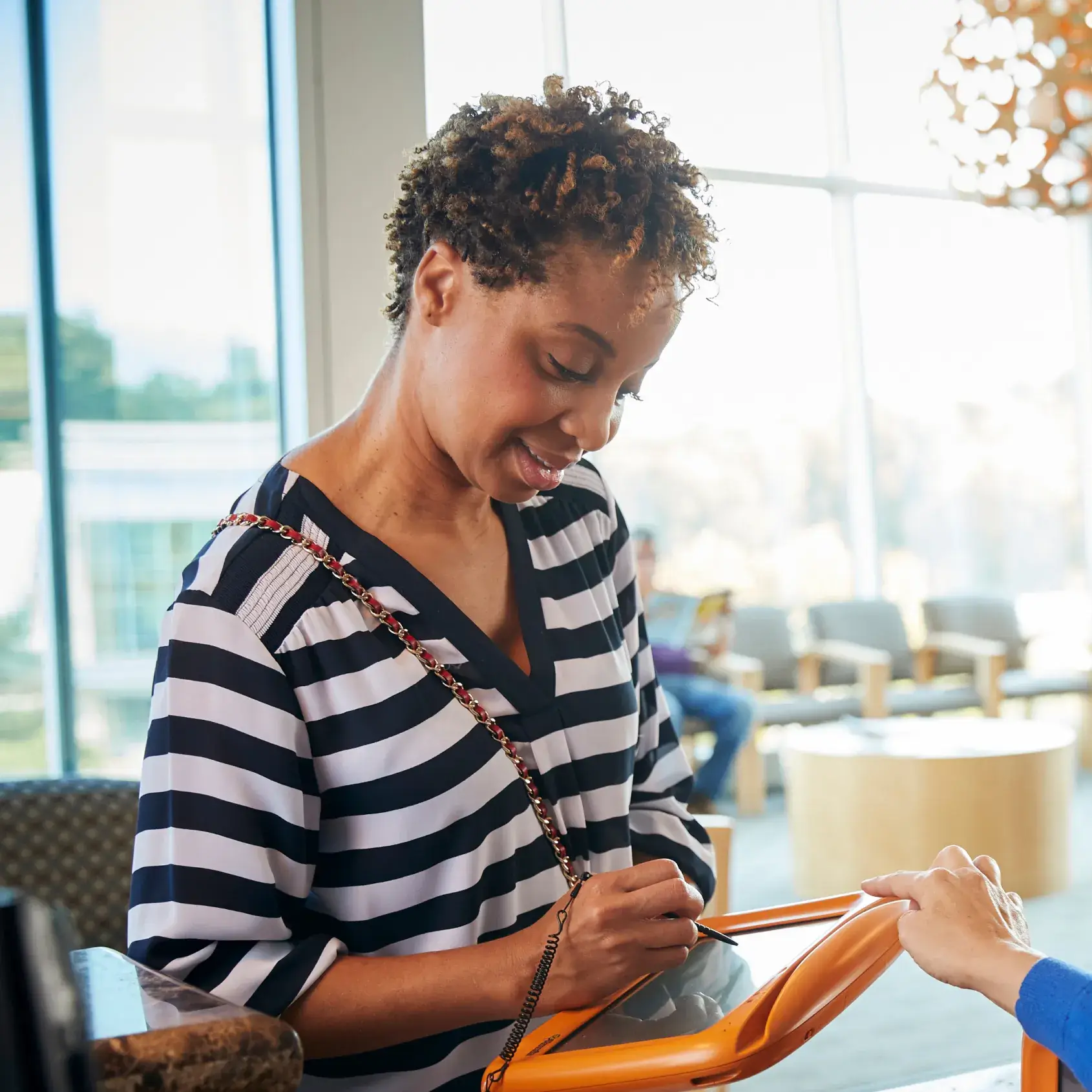A person in a striped shirt signs on an electronic device handed by another person.