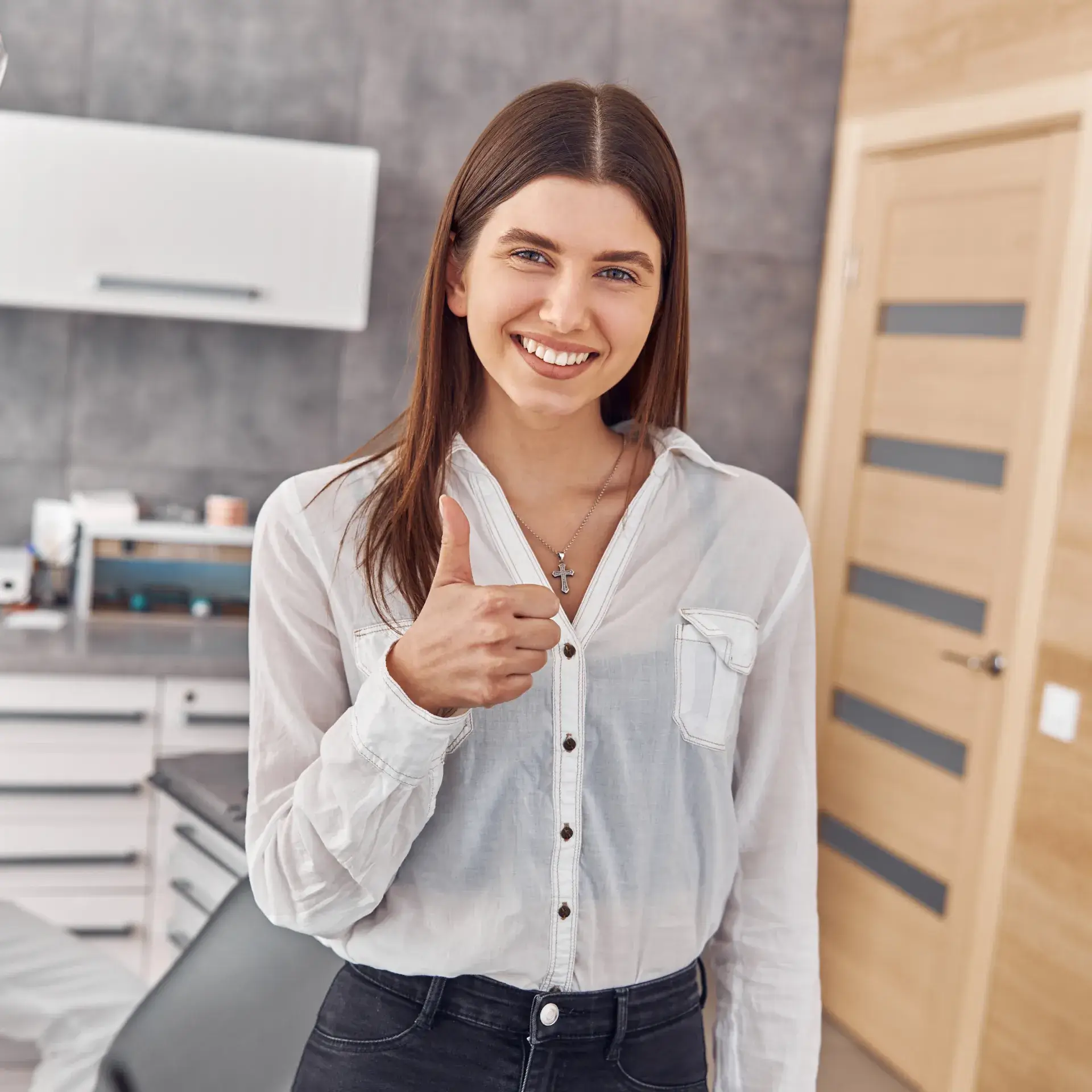 A woman in a white shirt gives a thumbs-up and smiles in a modern office.