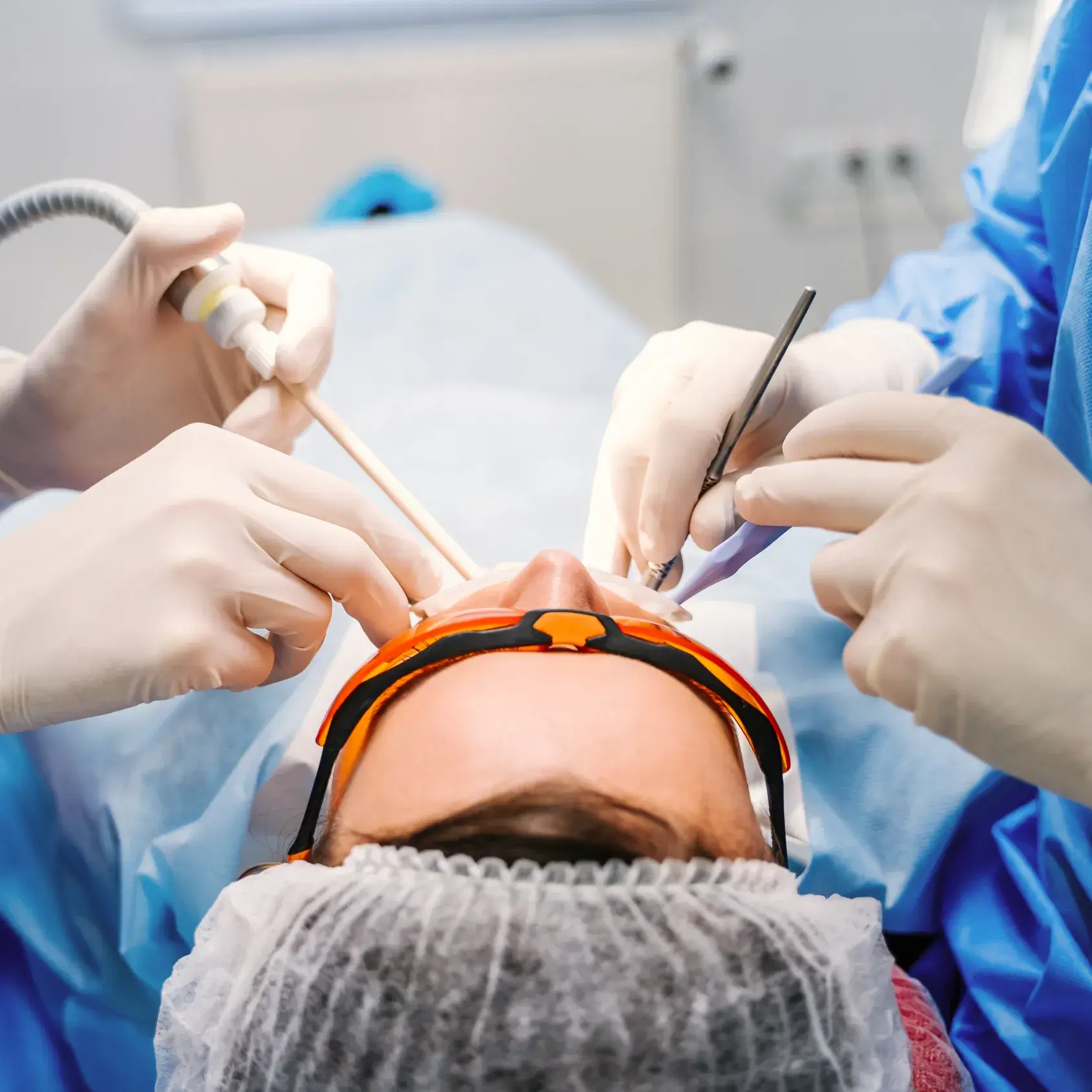 A dental professional performs a procedure in a clinic, using tools on a patient's teeth.
