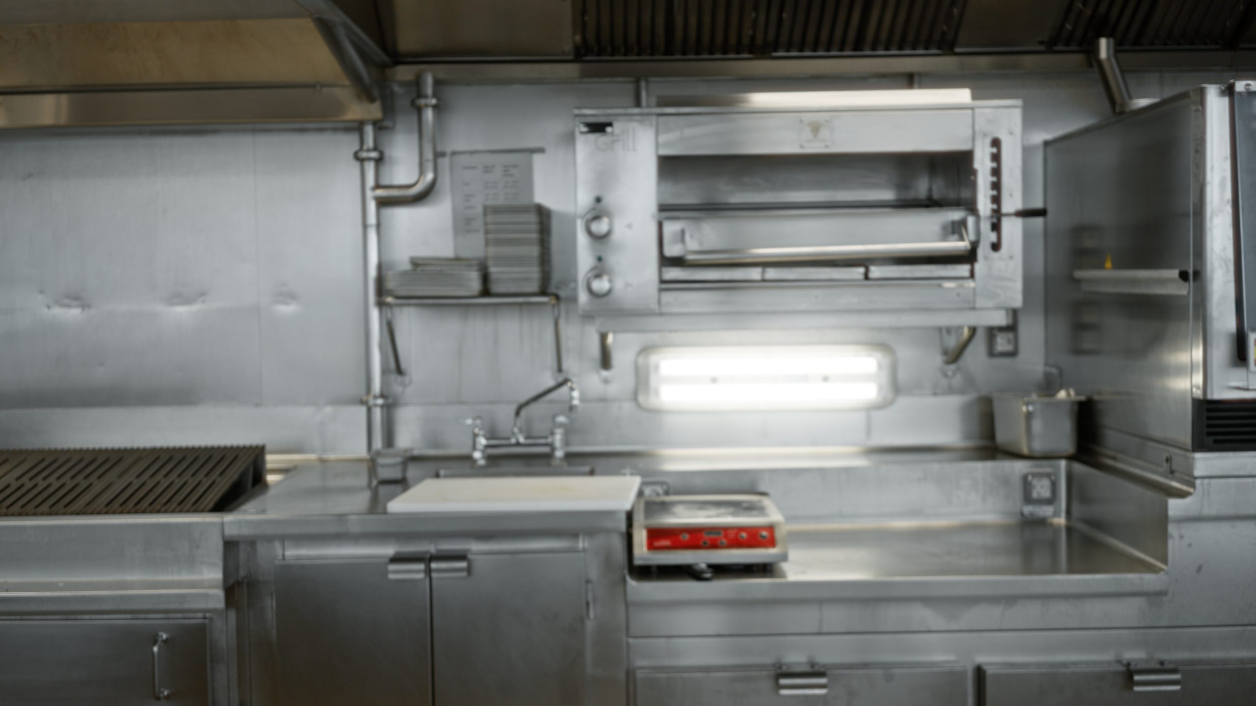 Commercial kitchen with stainless steel counters and appliances, soft blurred interior; background copyspace backplate template.