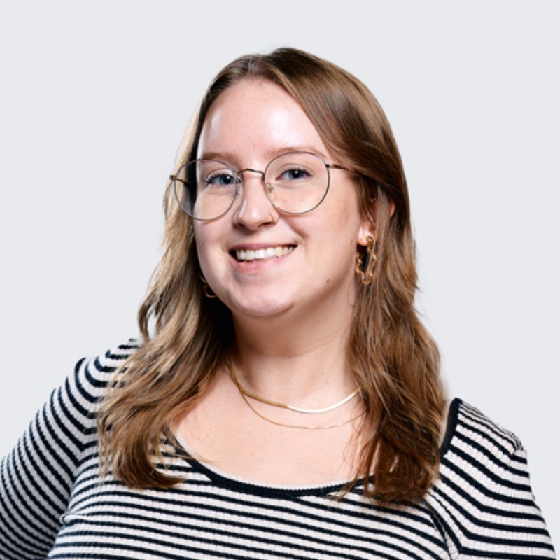 Smiling woman with light brown hair wearing round glasses and a black-and-white striped top.