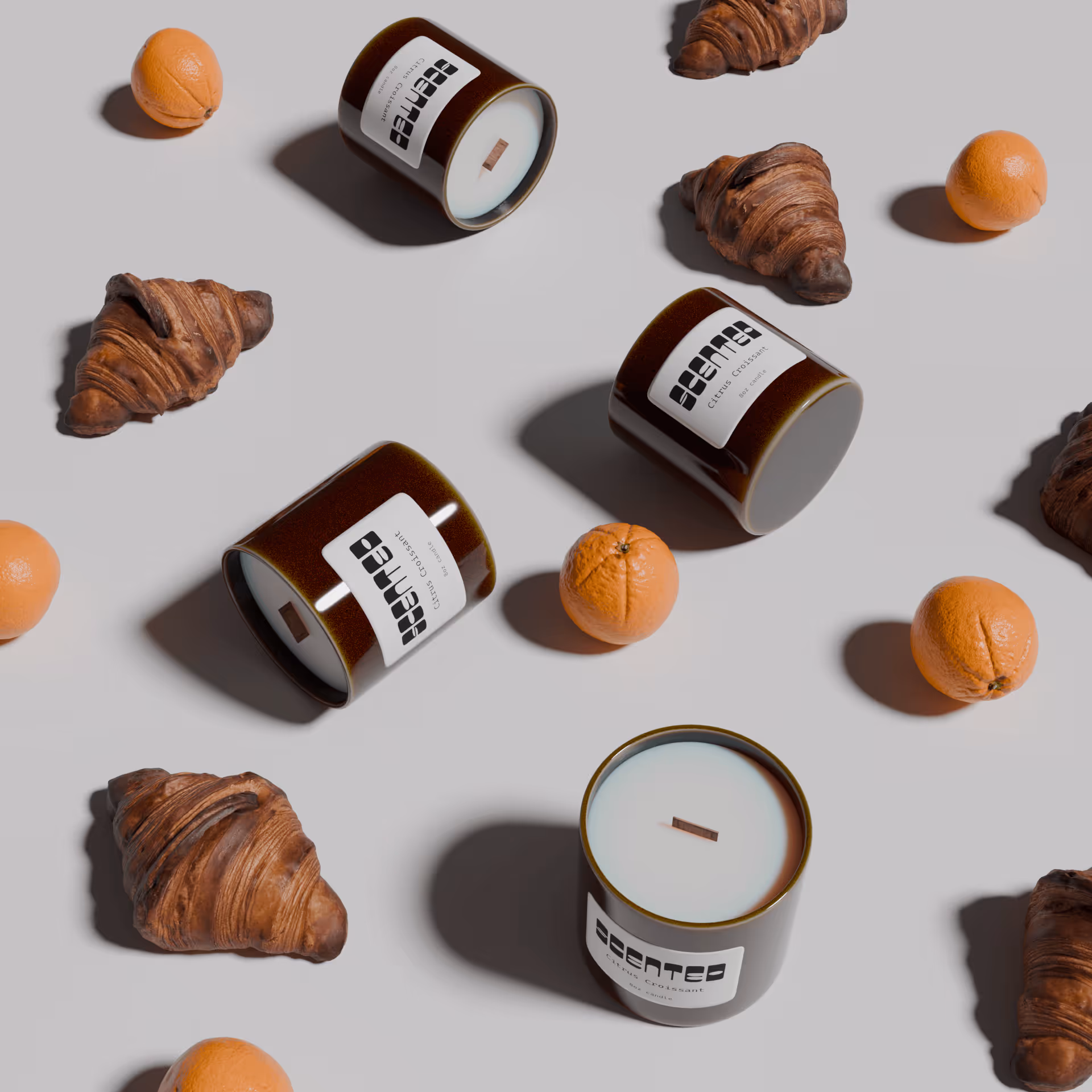 Flat lay of dark brown scented candles labeled 'citrus croissant' with fresh oranges and croissants on a light gray background.