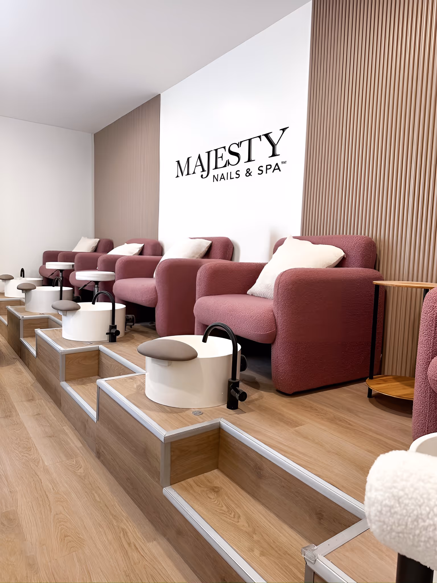 Interior of Majesty Nails & Spa with mauve armchairs, white pedicure bowls, and wooden flooring.