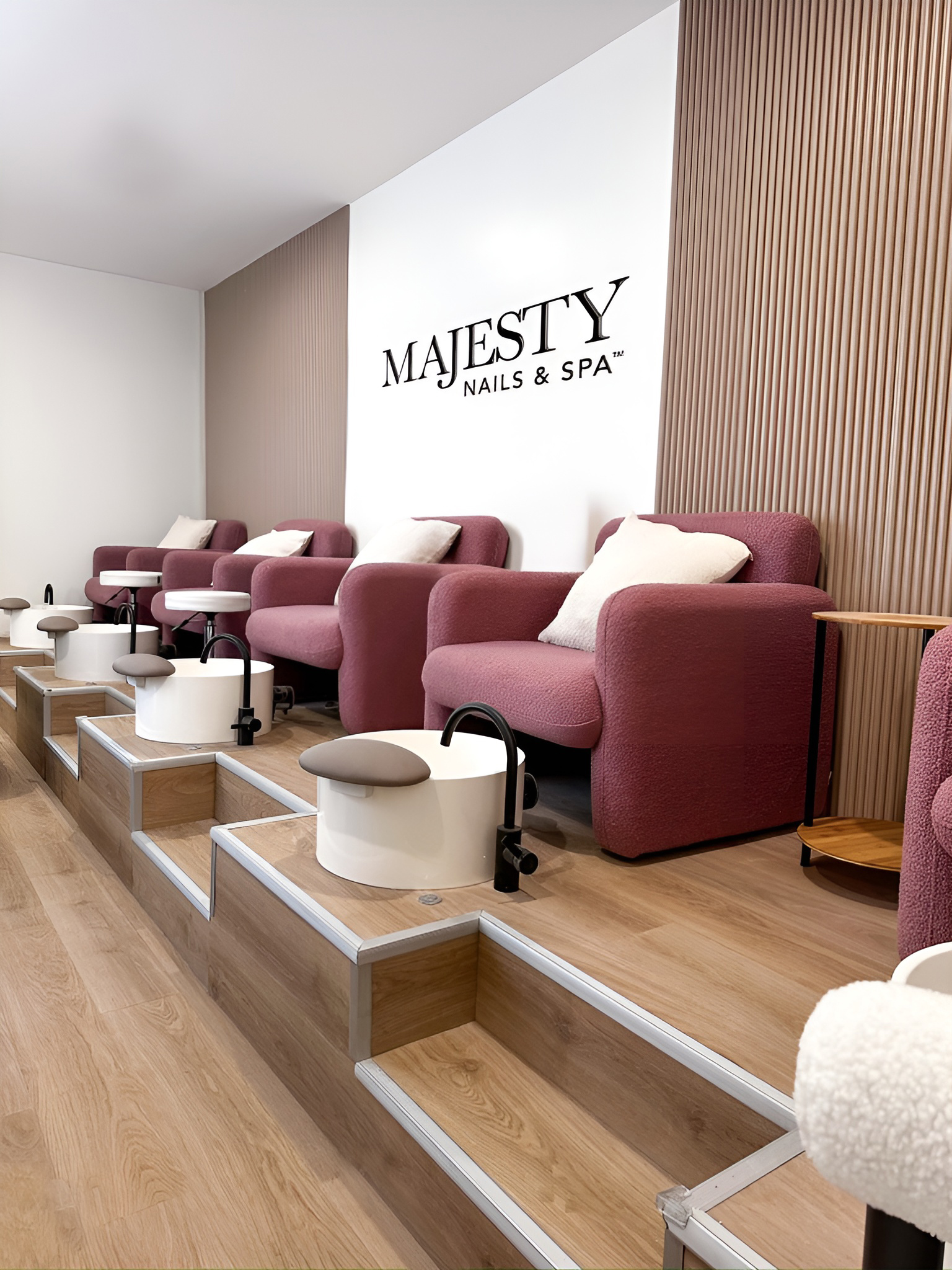 Interior of Majesty Nails & Spa with mauve armchairs, white pedicure bowls, and wooden flooring.