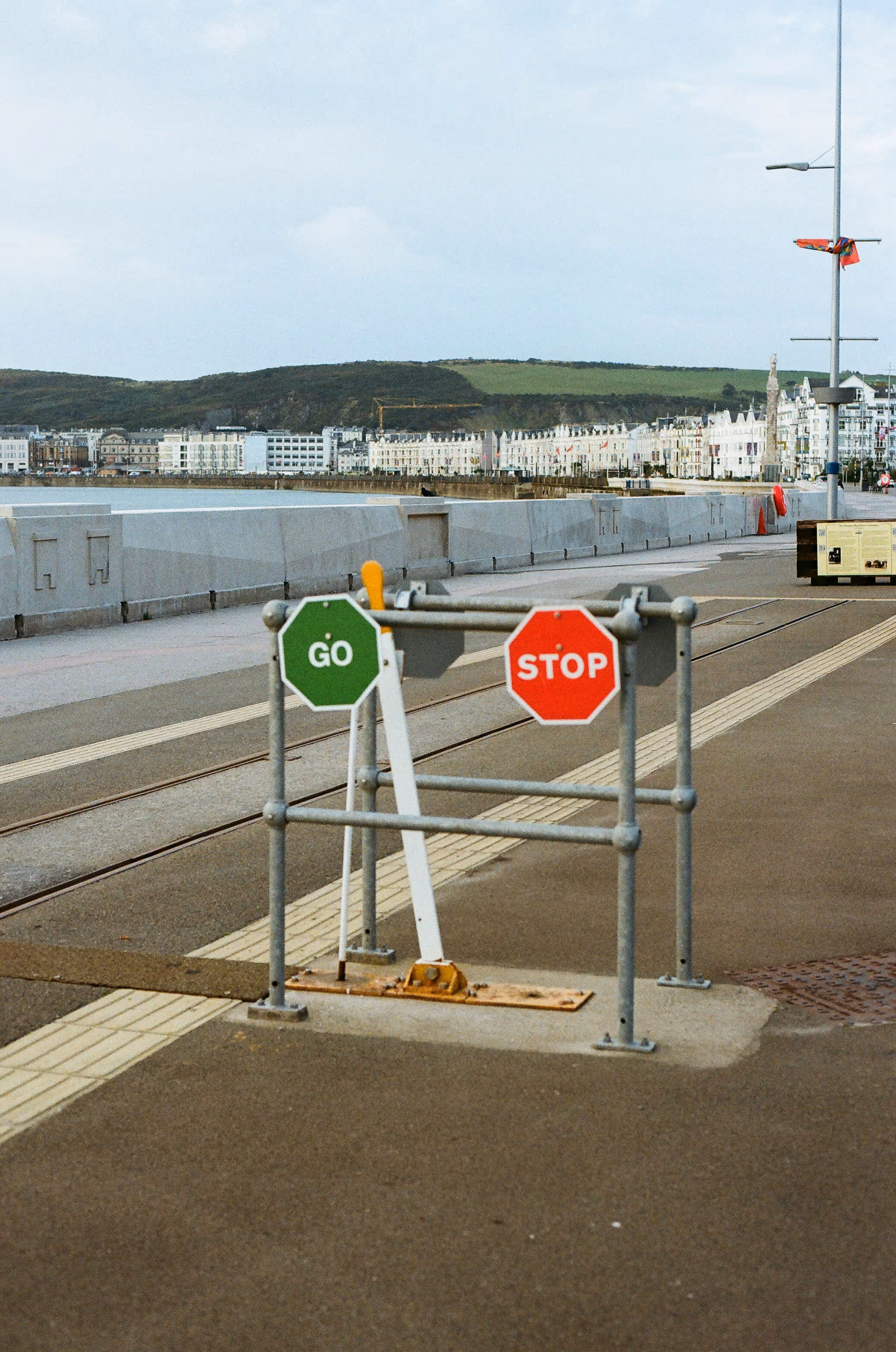Pedestrian gate with 'GO' and 'STOP' signs near waterfront rail tracks.
