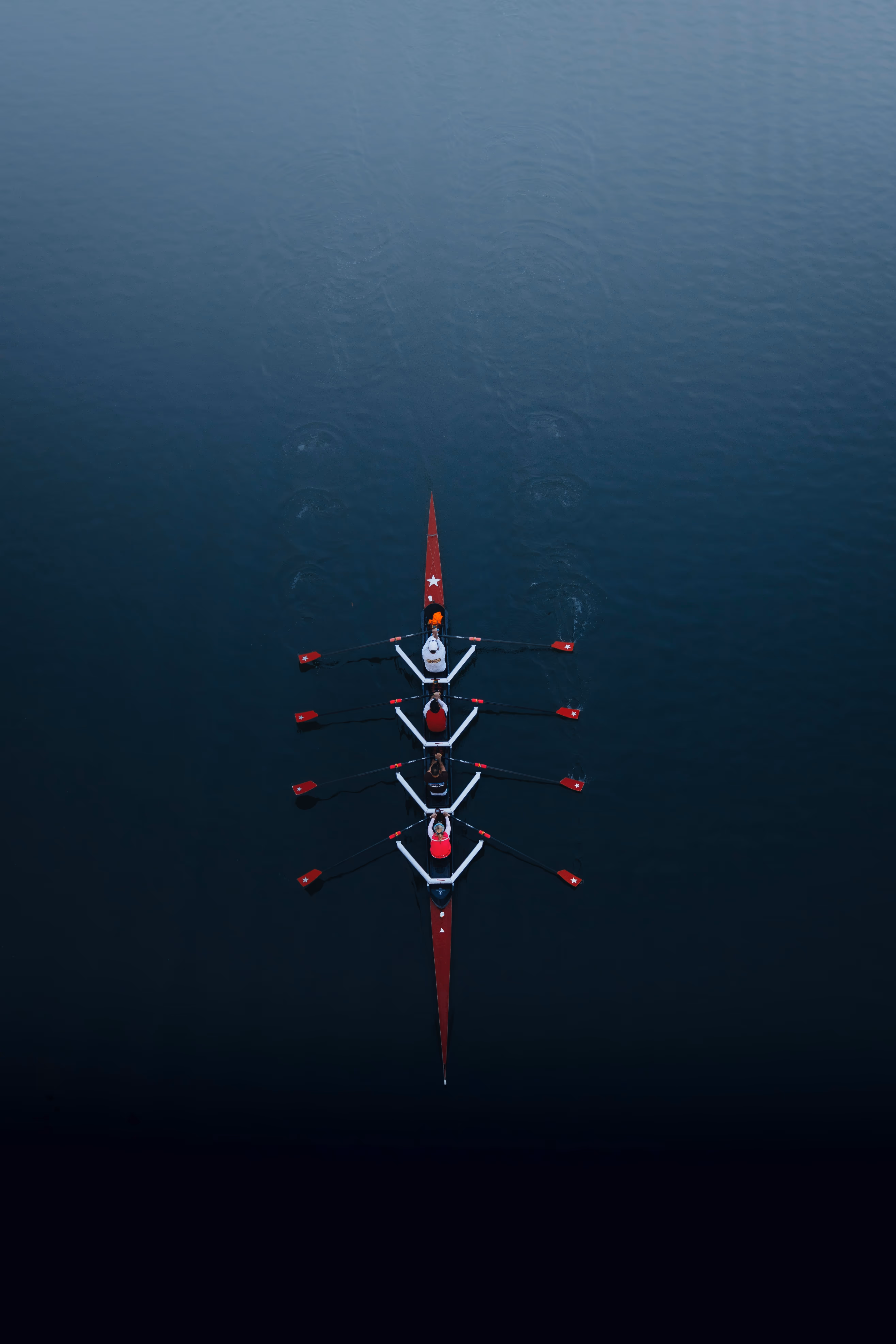 Aerial view of red rowing boat with four synchronized rowers on calm water.