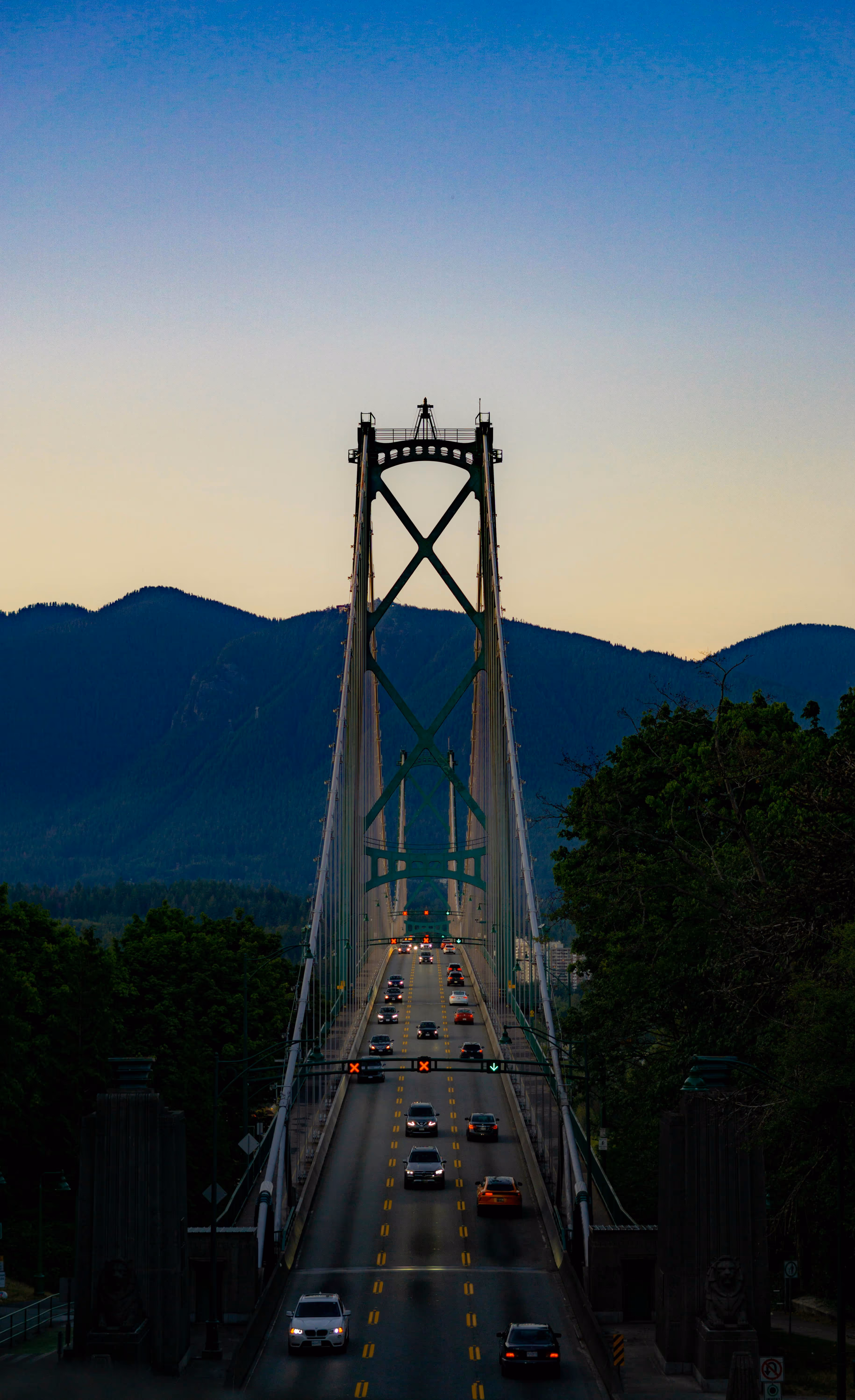 Suspension bridge with vehicles against mountain backdrop at sunrise or sunset.