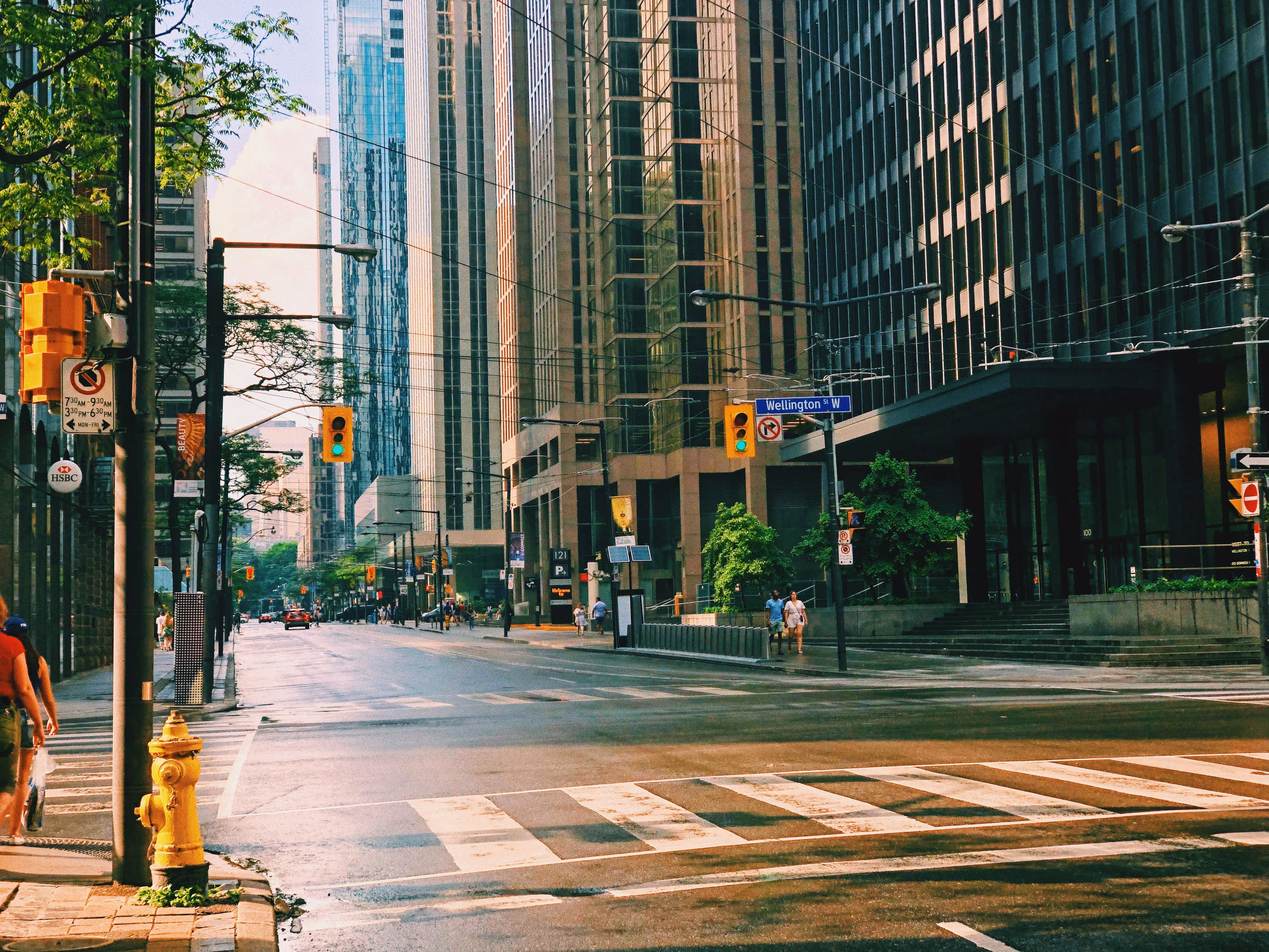 Wet city intersection with tall buildings, traffic lights, and pedestrians.