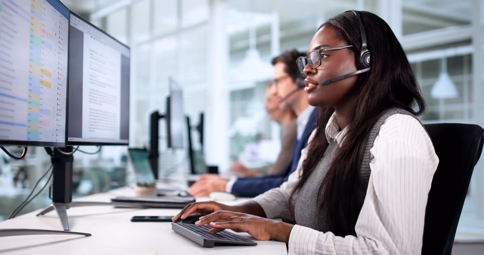 Customer service representatives wearing headsets working at computers in a bright office.