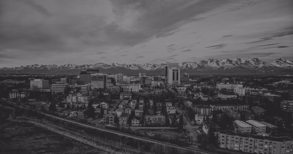 Anchorage city skyline with tall buildings in front of a mountain range under a cloudy sky. Represents Alaska's At-large Congressional District.