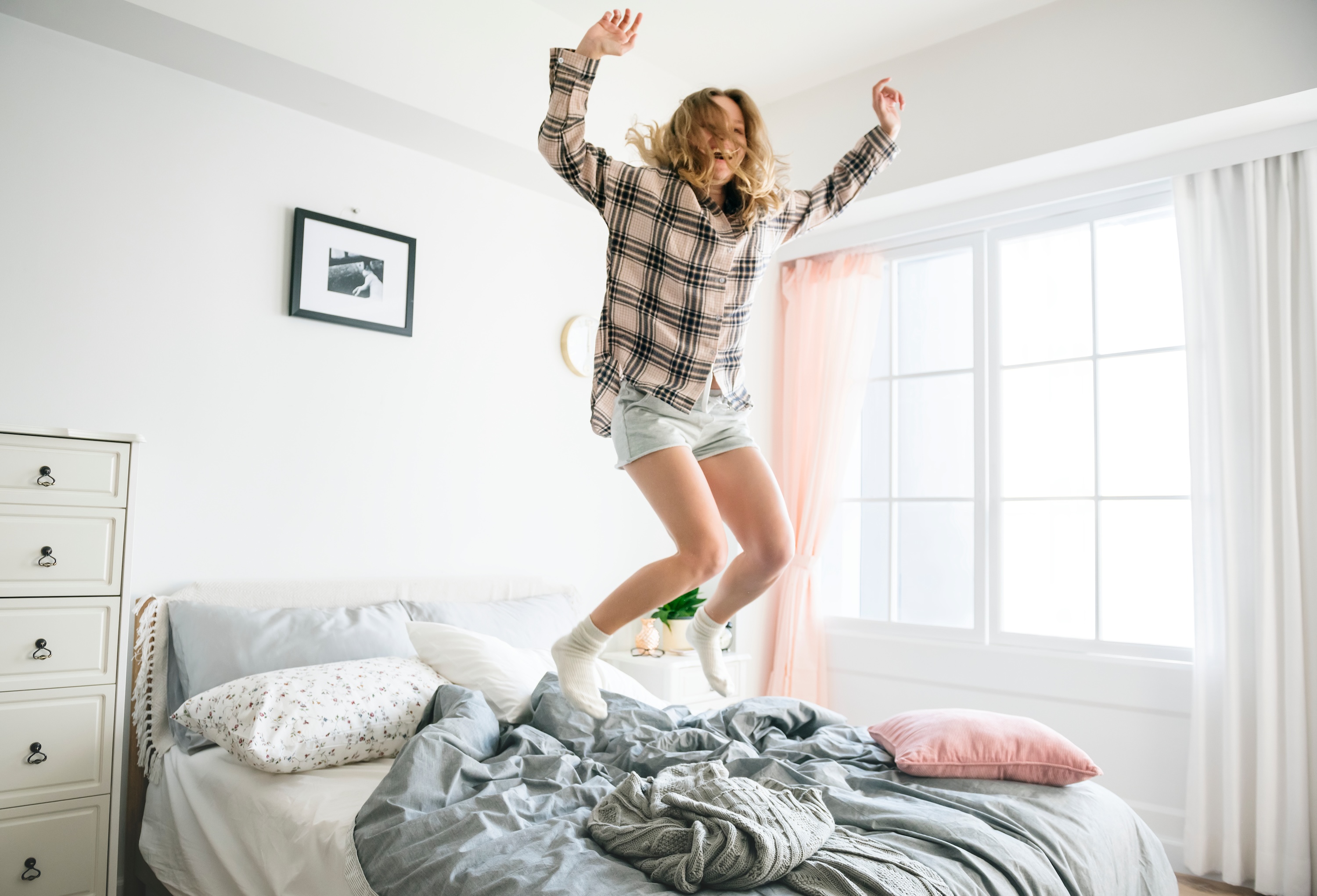 Resident jumping on a bed inside a bright apartment bedroom