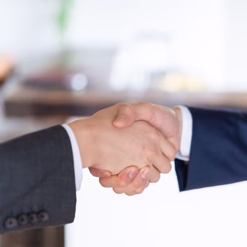 Two business professionals shaking hands in a modern office setting, symbolizing agreement and collaboration.