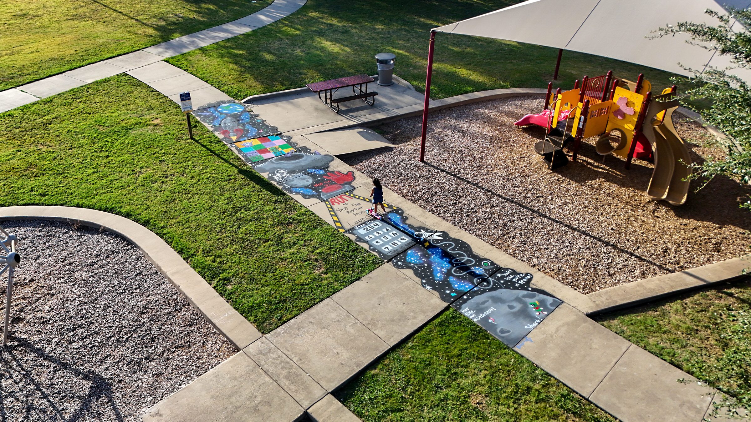 Aerial view of a colorful space-themed sidewalk obstacle course beside a playground at South Waco Recreation Center.
