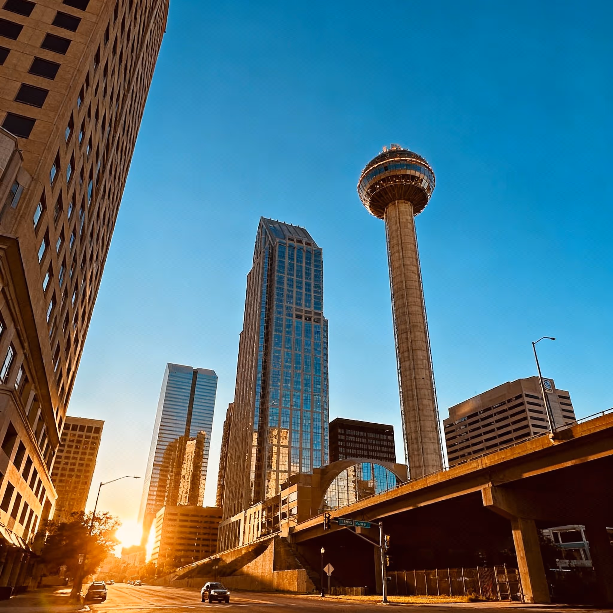 Dallas skyline at sunset featuring the Reunion Tower and surrounding skyscrapers under a clear blue sky.